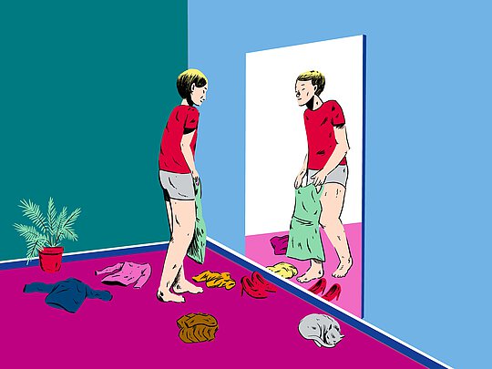 Eine Trans*person steht vor dem Spiegel und probiert verschiedene Kleidungstücke an.