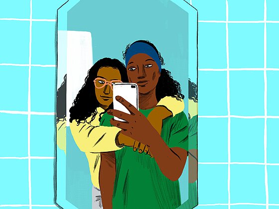 Zwei LSBTIQ BIPoCs machen ein Selfie vor einem Spiegel, die hintere Person umarmt die vordere. 